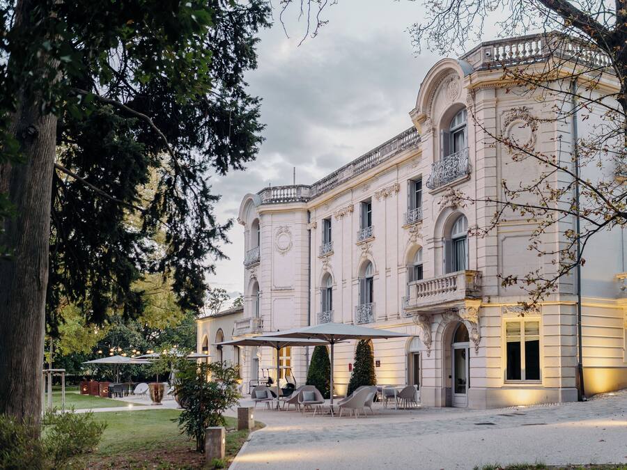 Un edificio imponente de arquitectura clásica, con un amplio patio con asientos al aire libre y un jardín bien cuidado.