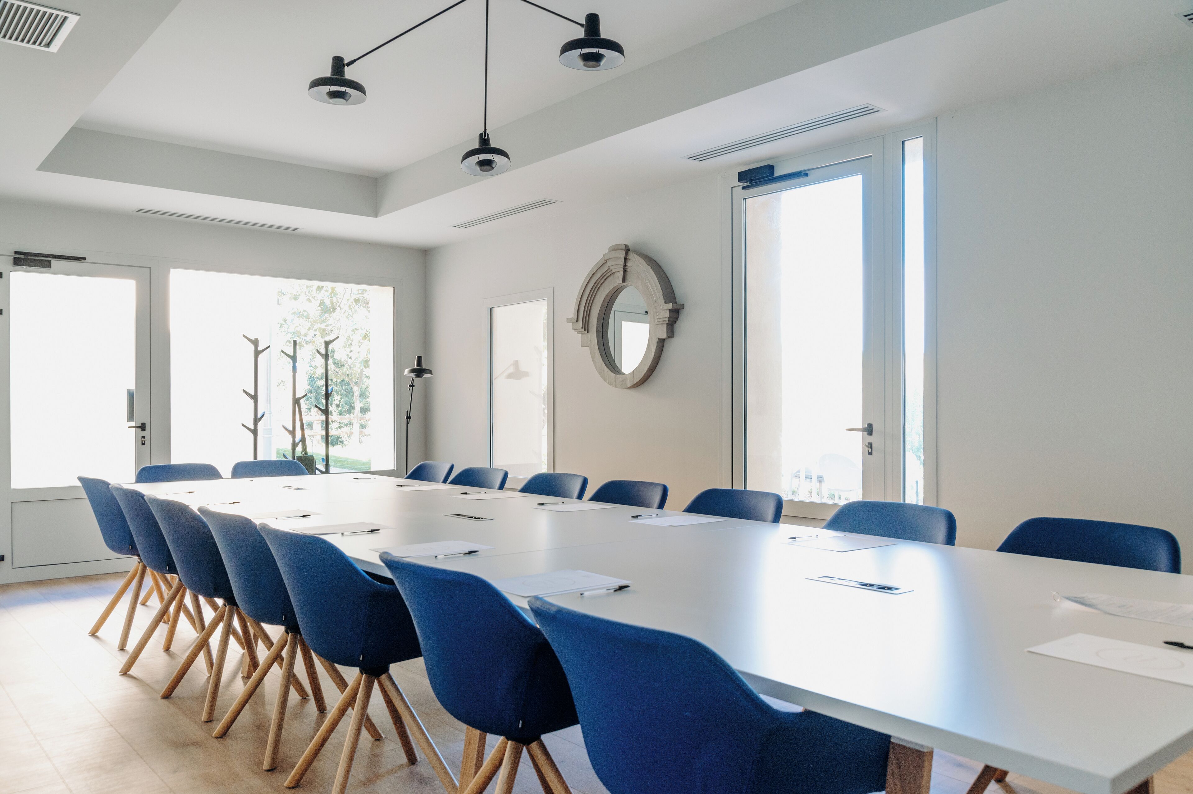 A conference room with a long table, blue chairs, and a large mirror on the wall.