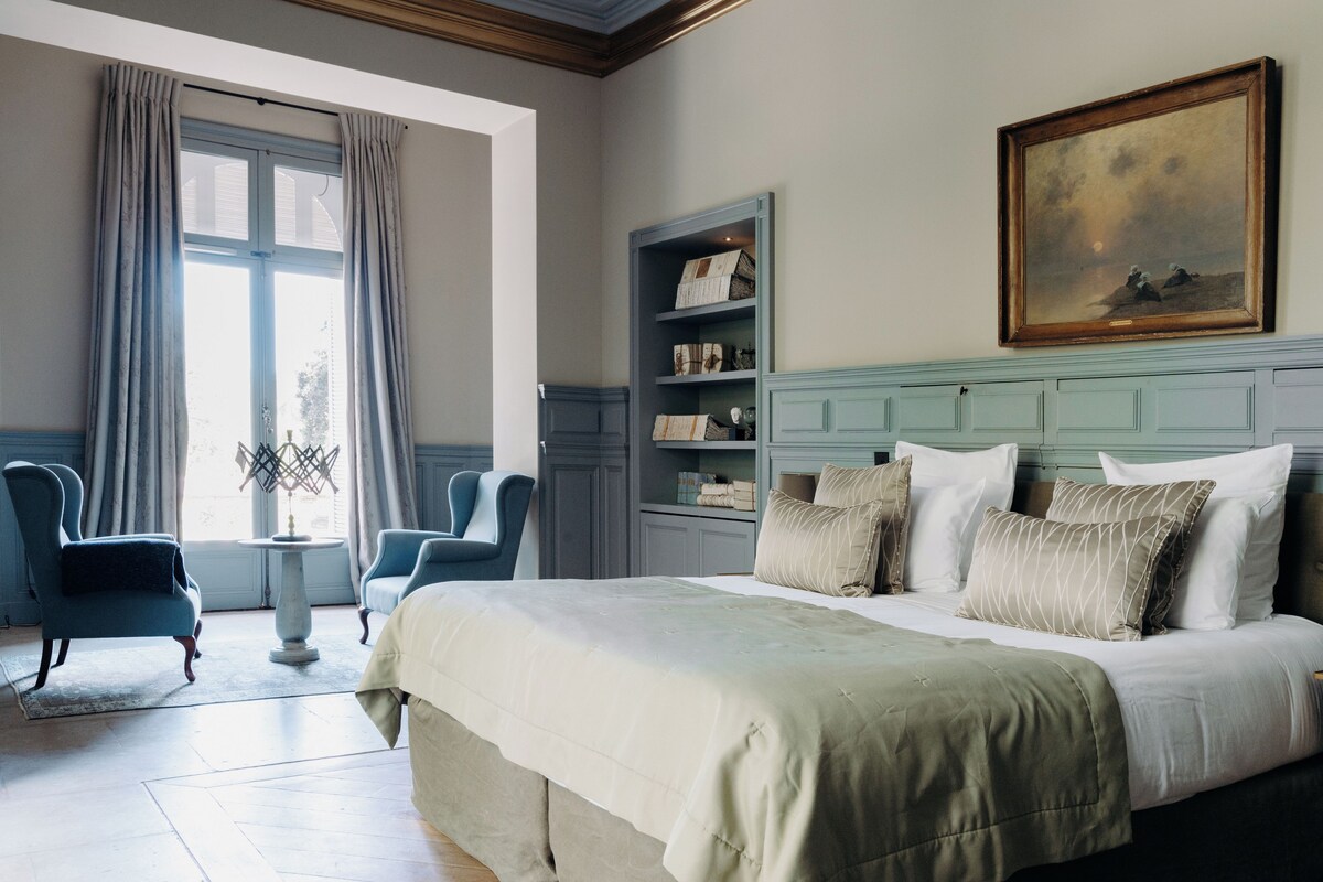 Un dormitorio con una cama grande, dos sillones, una mesita y una estantería.