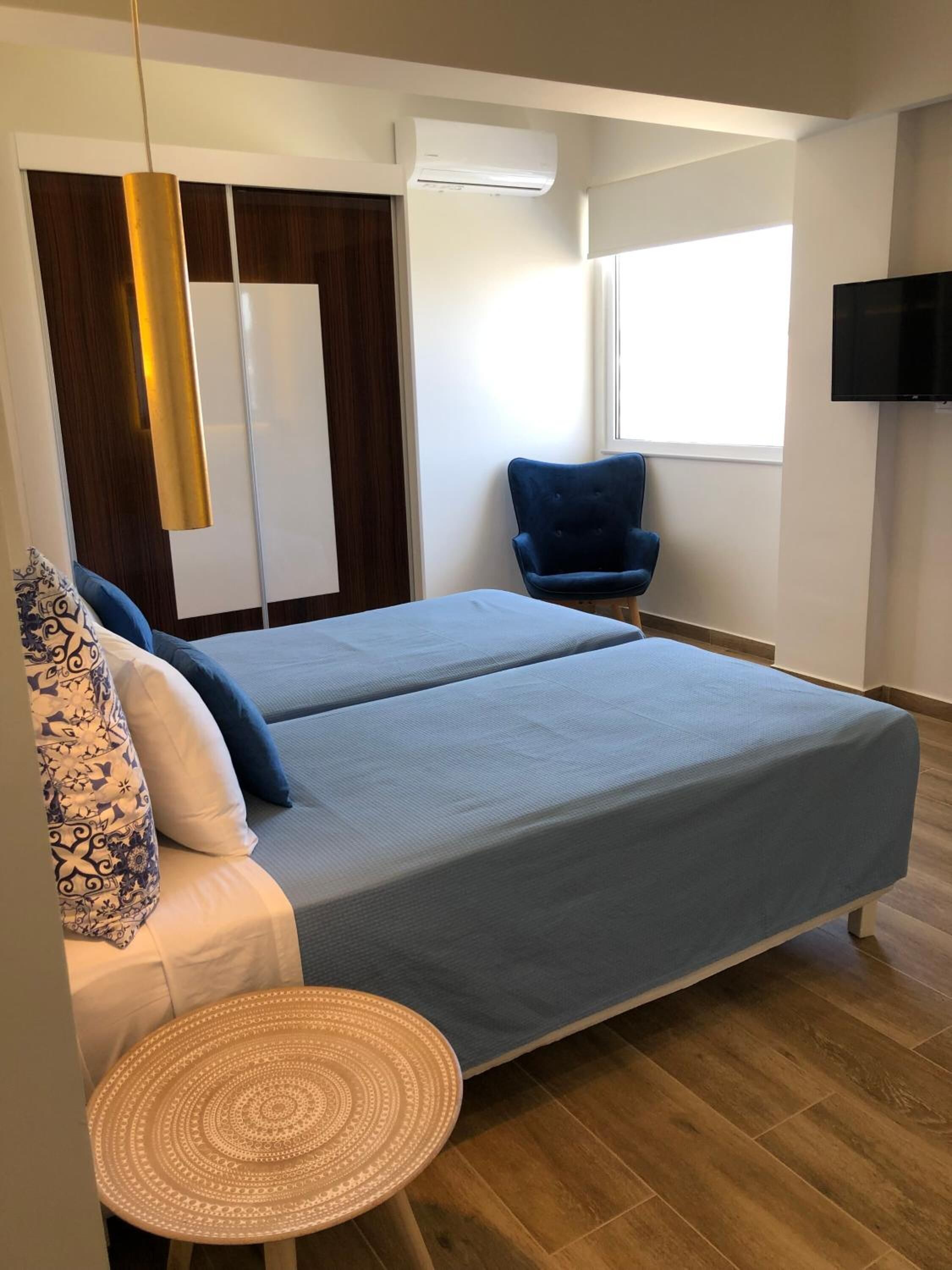 A modern bedroom with a bed, a blue chair, a small round table, and a TV mounted on the wall.