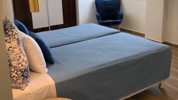A modern bedroom with a bed, a blue chair, a small round table, and a TV mounted on the wall.