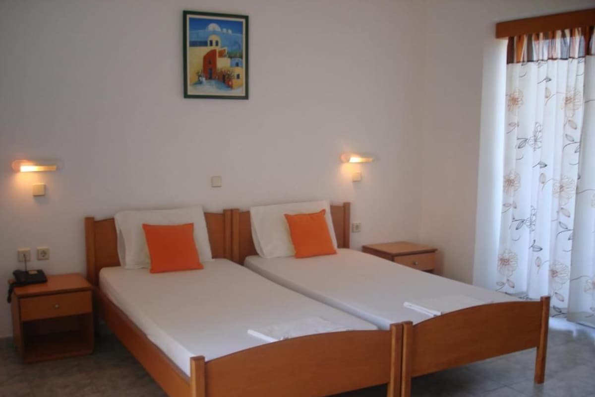 A double bed with two nightstands, each with a lamp, in a room with a painting on the wall and a floral curtain.
