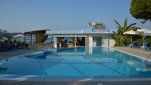 Een zwembadgedeelte met ligbedden, een poolbar en een gebouw met de tekst 'ELPIDA BEACH STUDIOS'.