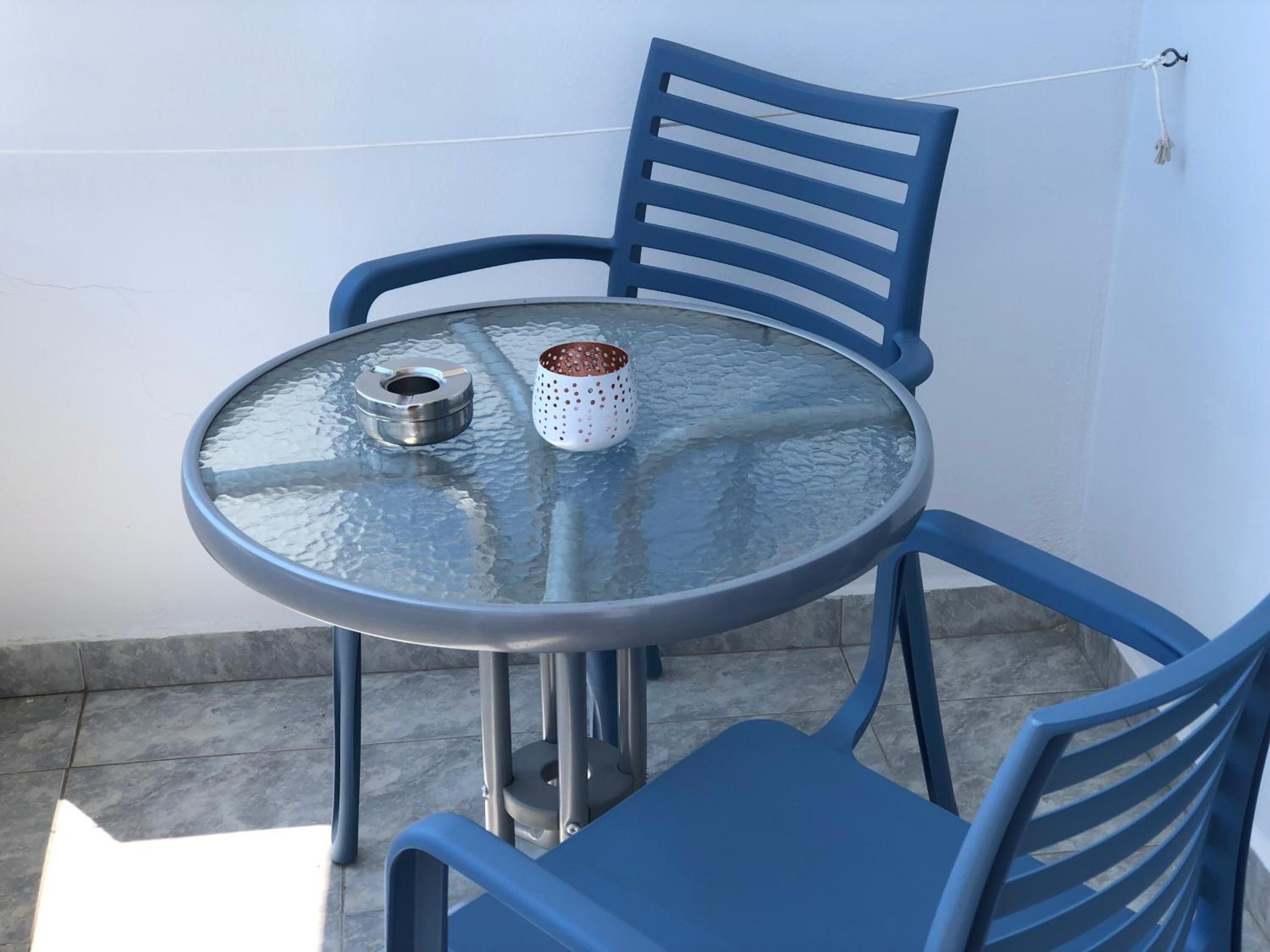 Une table ronde en verre avec des pieds en métal, accompagnée de deux chaises bleues.