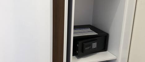 A white wardrobe with a wooden panel on the left, a black electronic device on the middle shelf, and a white appliance with a green sticker on the bottom shelf.