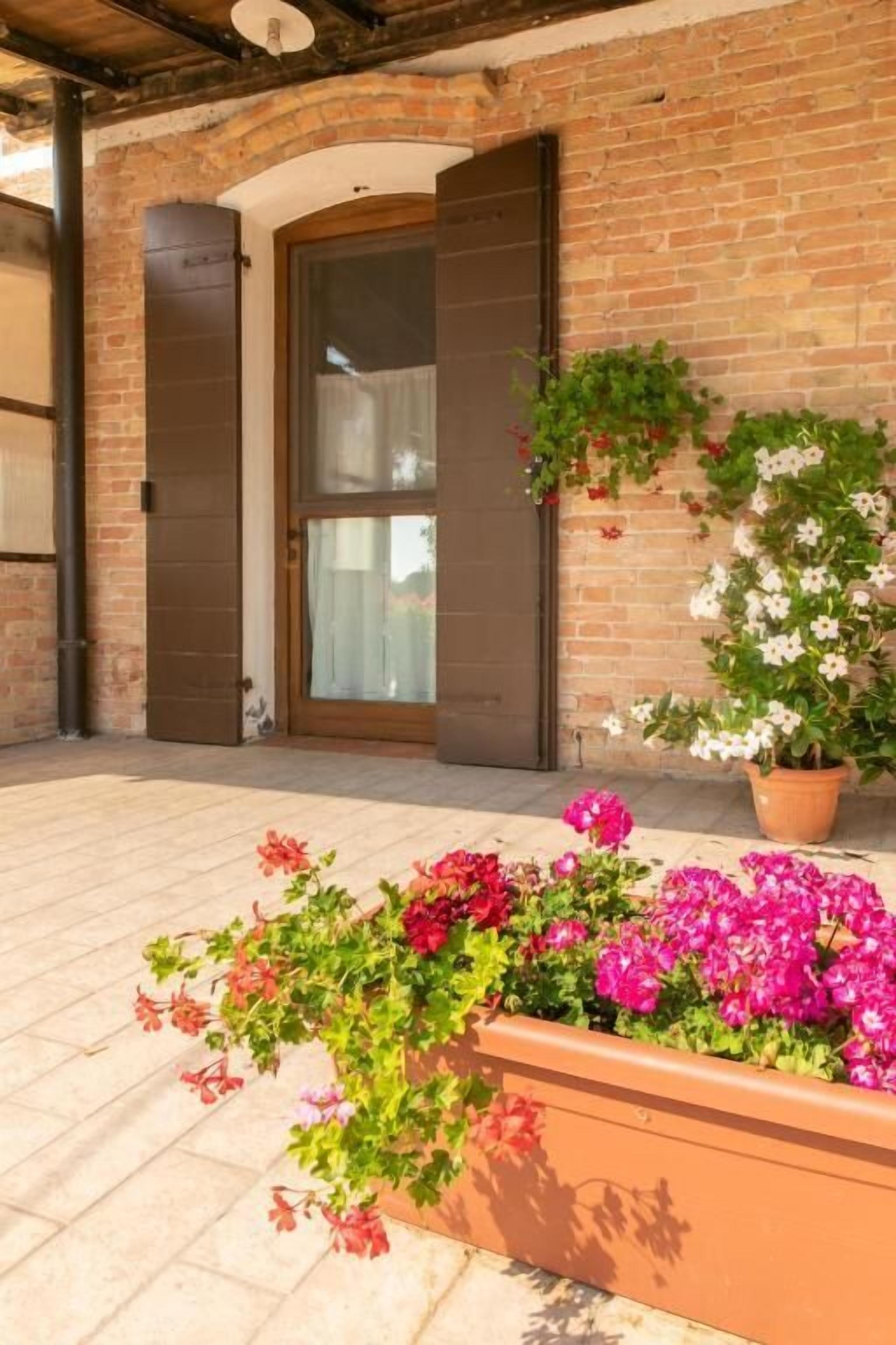 A brick building with a large glass door, a flower planter with pink and red flowers, and a hanging plant with white flowers.