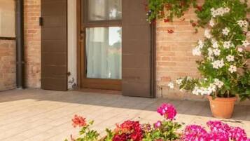 A brick building with a large glass door, a flower planter with pink and red flowers, and a hanging plant with white flowers.
