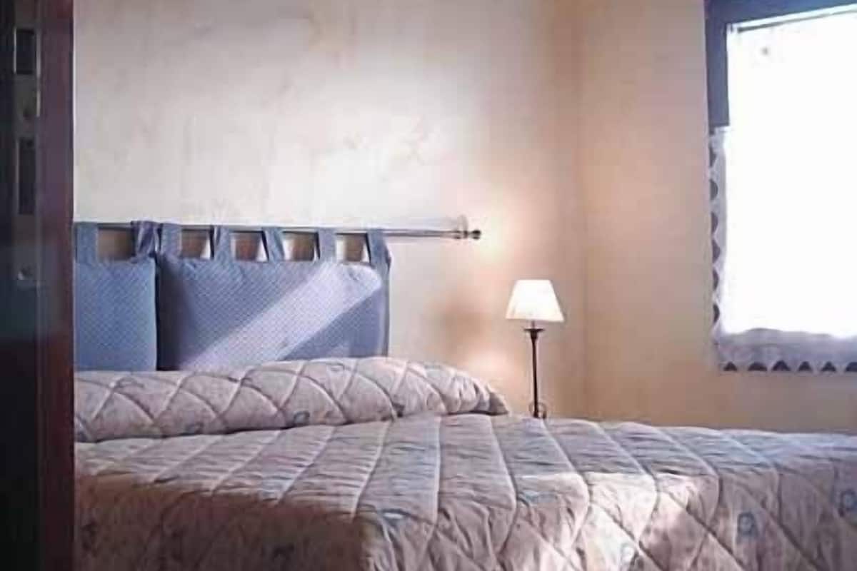 Ein Schlafzimmer mit einem Bett, einem Nachttisch, einer Lampe und einem Fenster mit Blick.