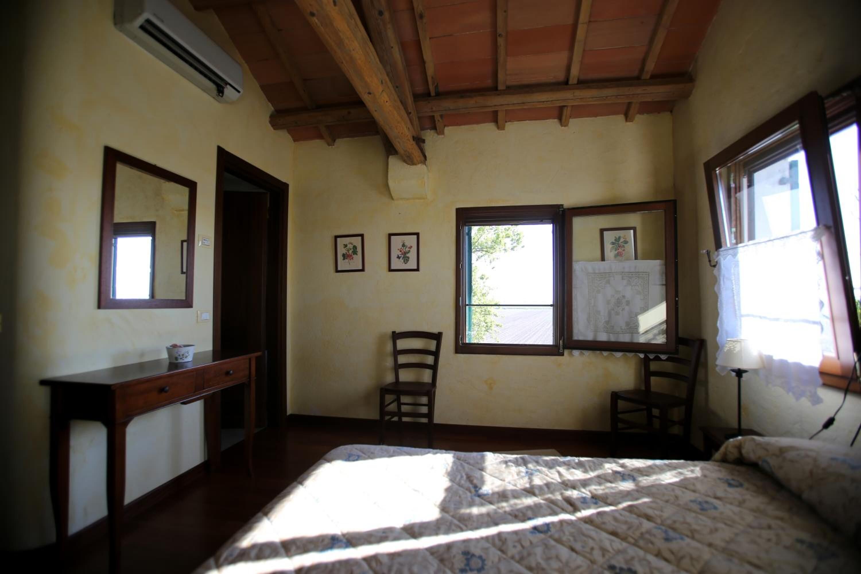 A bedroom with a wooden bed, a nightstand, a chair, a desk, and a window with a view.