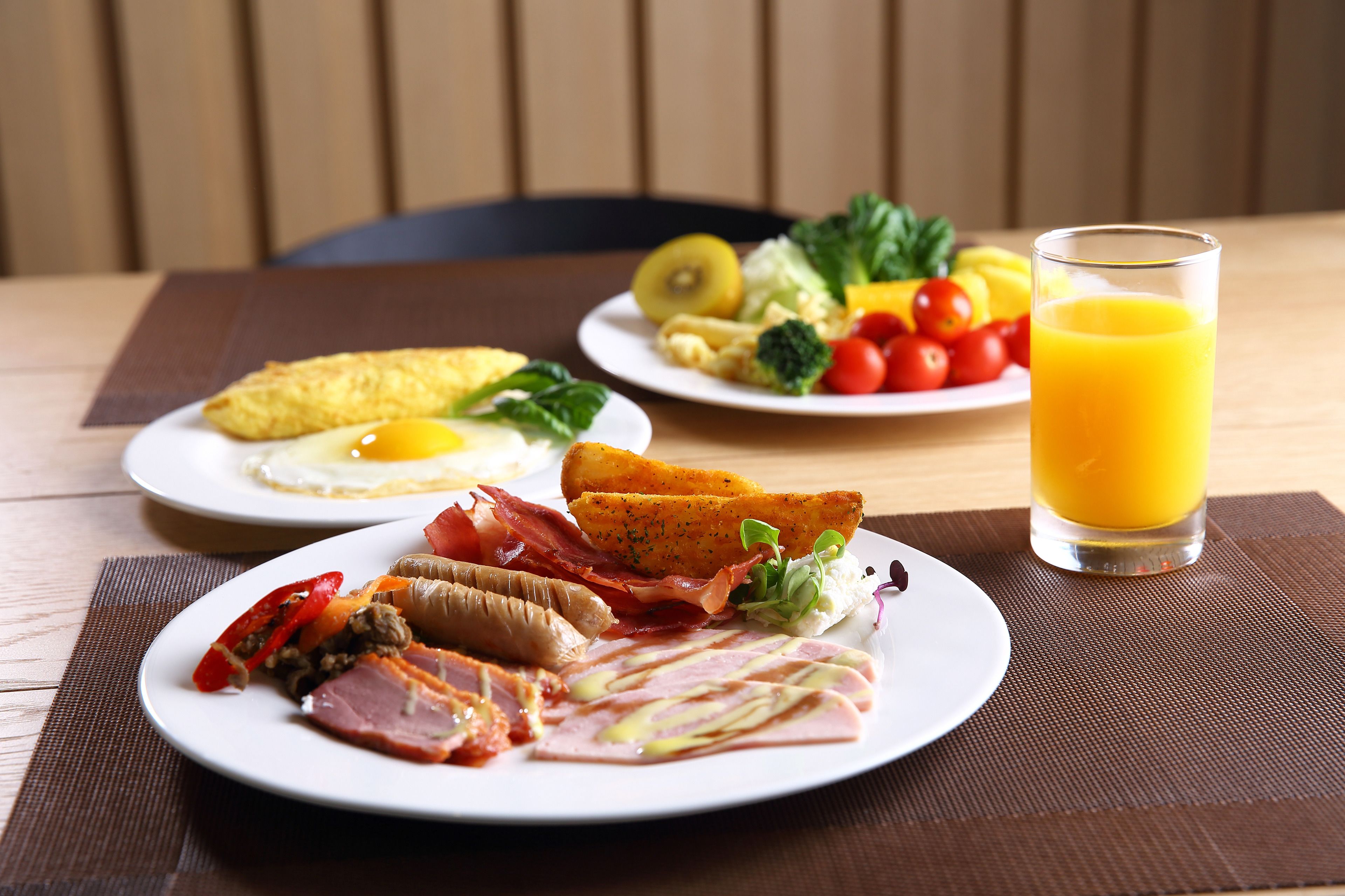 Une table en bois dressée pour le petit-déjeuner, avec des assiettes remplies de nourriture et un verre de jus d’orange.