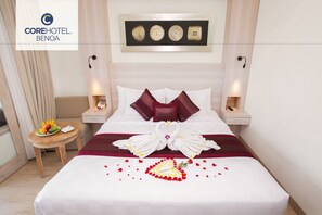 A hotel room with a neatly made bed, a small table with fruit, and a wall art piece above the bed. - Core Hotel Benoa (Nusa Dua)