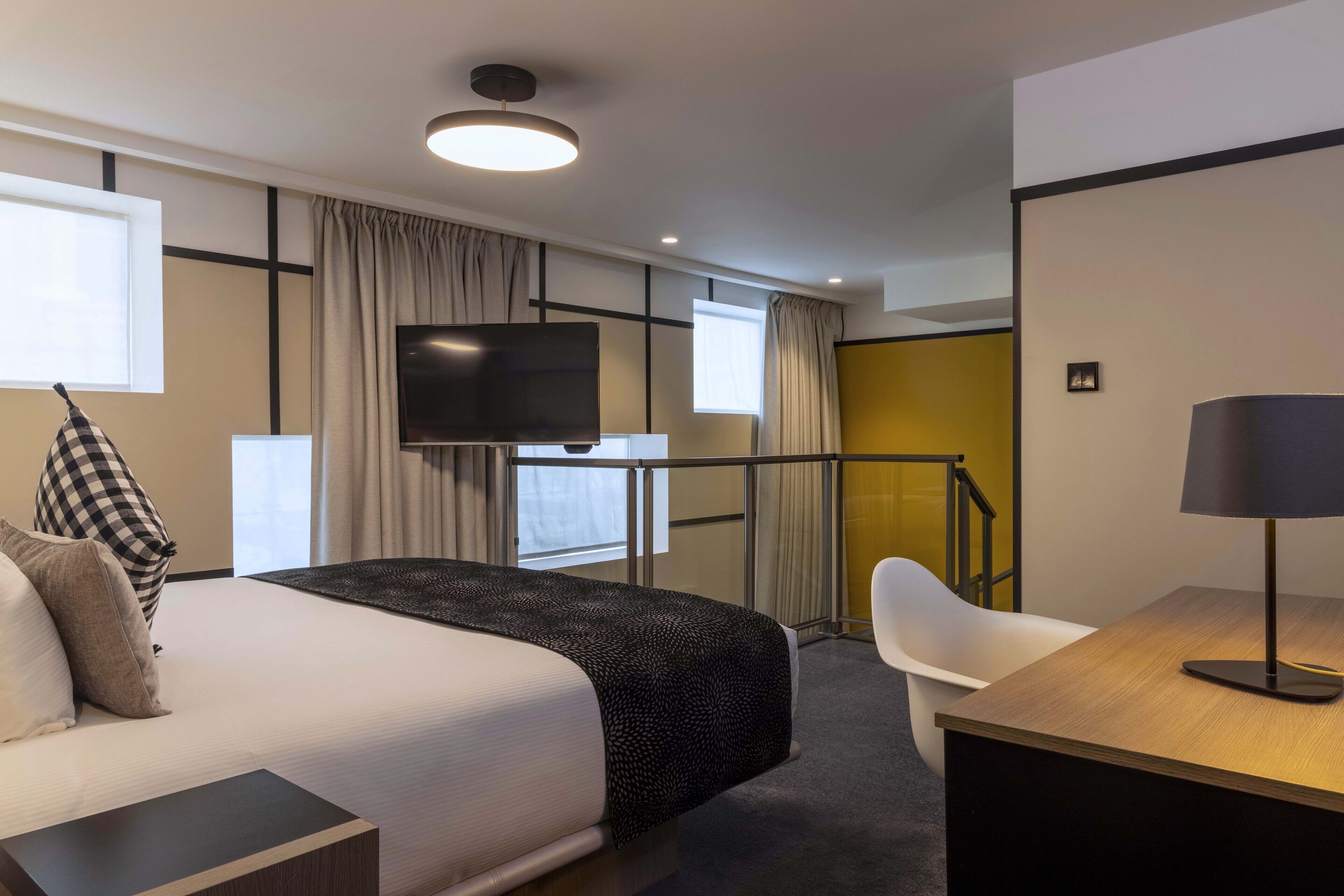 A hotel room with a bed, a desk, a chair, a TV, and a staircase.