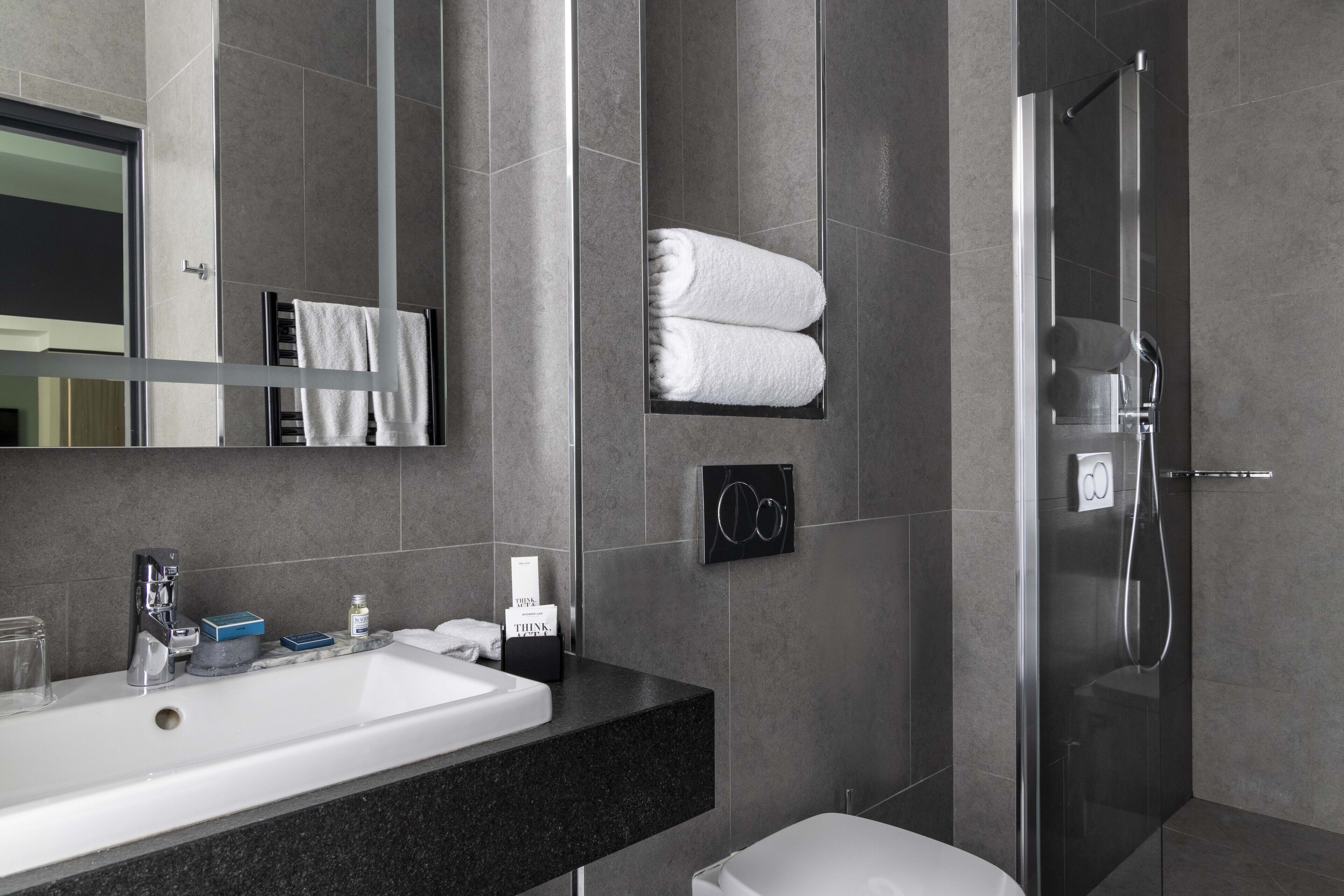 Une salle de bain moderne avec un grand miroir, un lavabo, une douche en verre et des serviettes soigneusement pliées, disposées sur le mur.