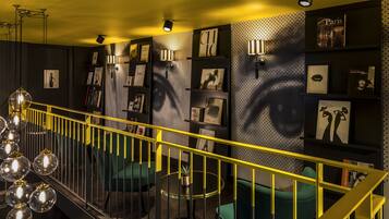 Un interior moderno con barandilla amarilla, asientos verdes y estanterías de pared con fotografías y libros enmarcados.