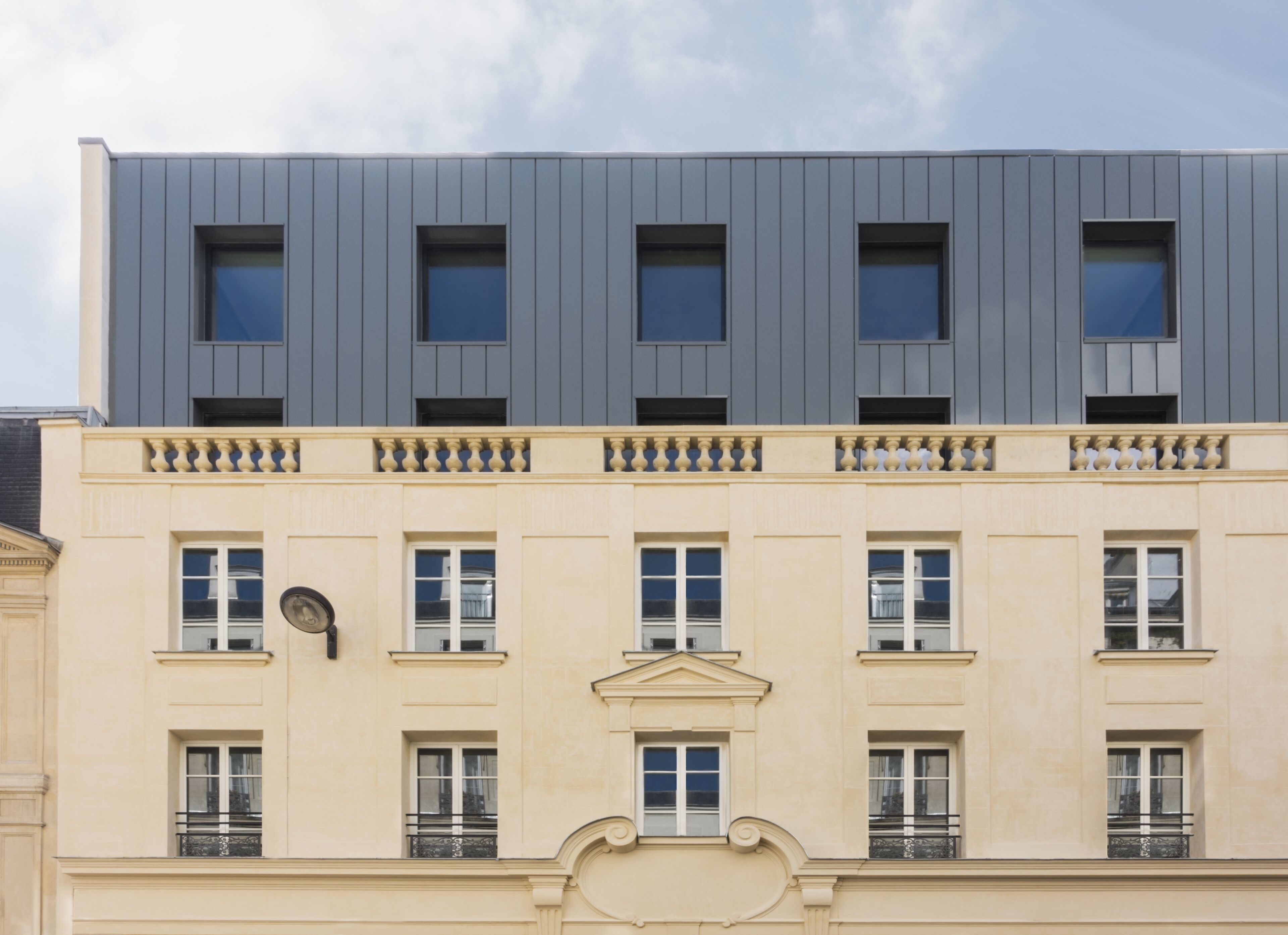 A building with a modern upper section and a classical lower section, featuring multiple windows and balconies.