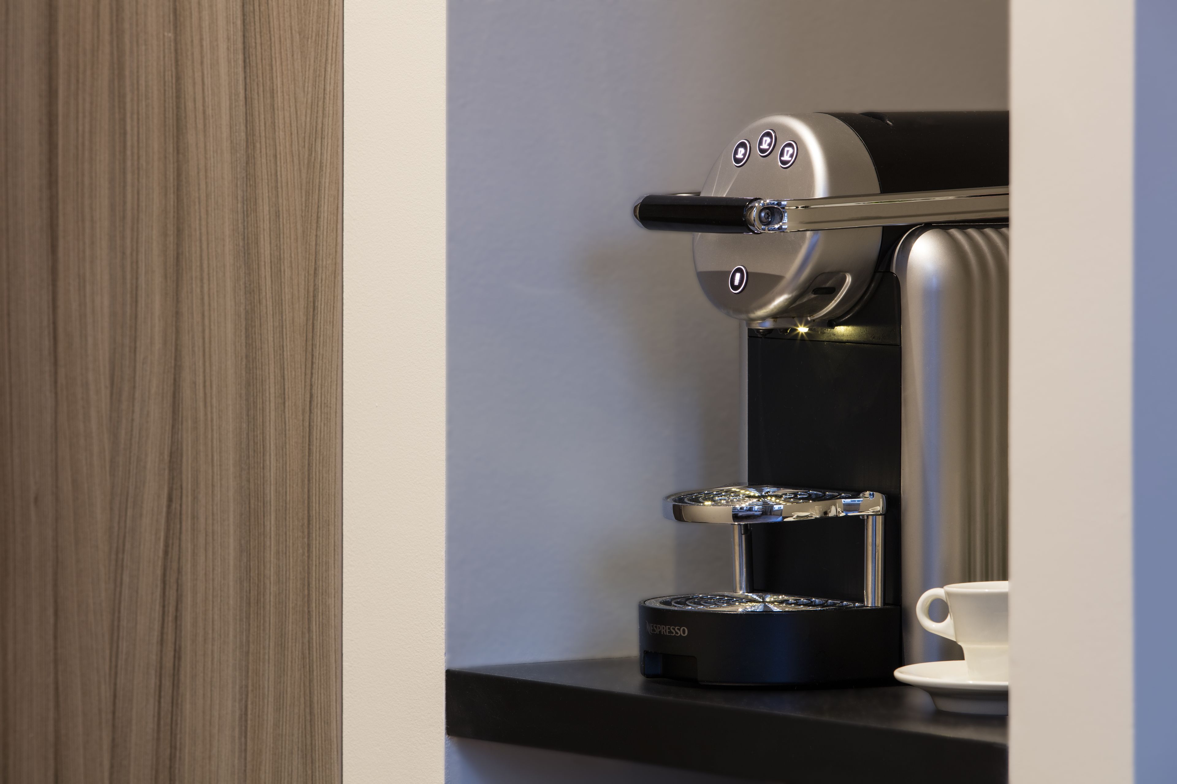 A modern espresso machine with a digital interface, a cup of coffee on the right, and a wooden panel on the left.