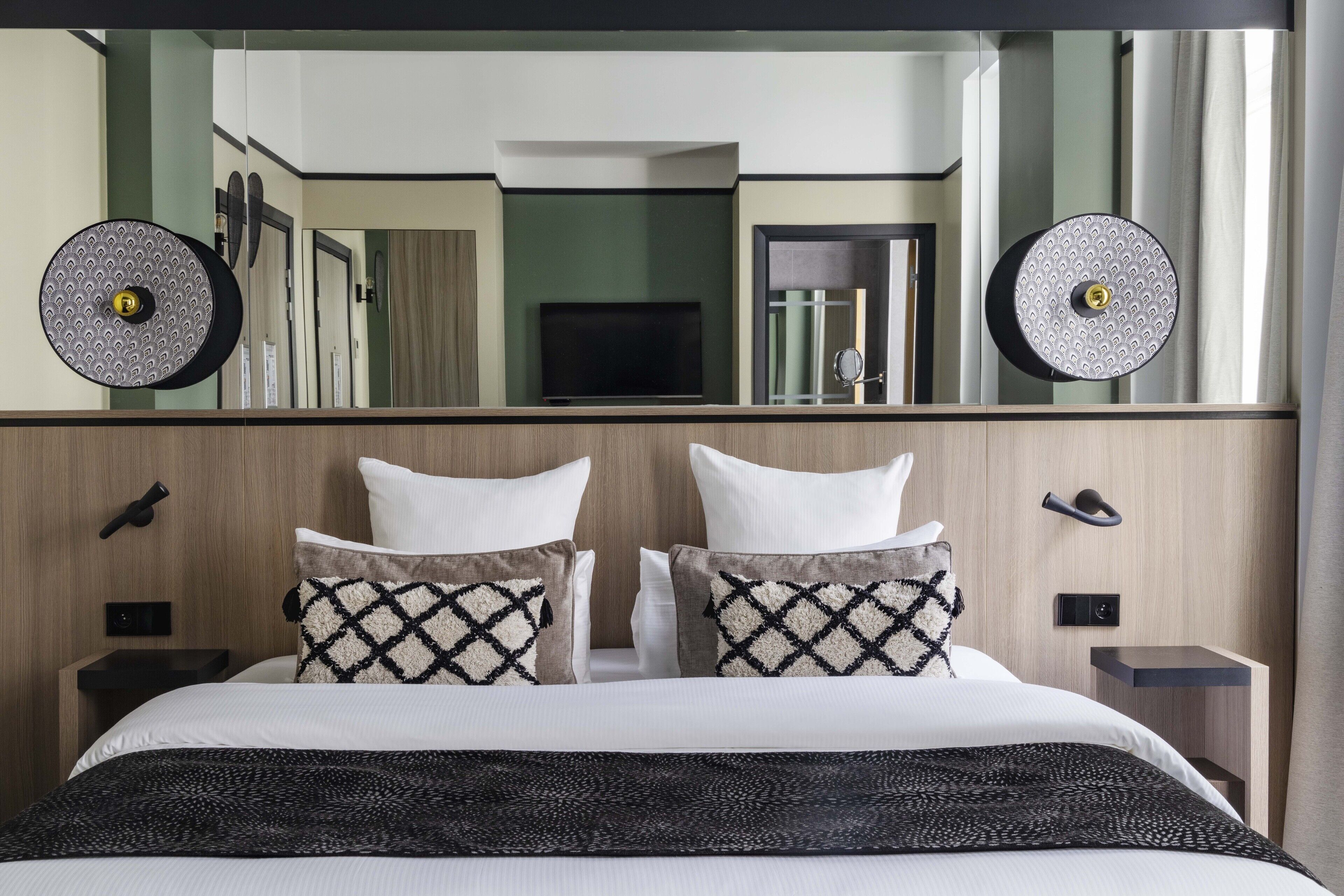 A hotel room with a large bed, two bedside tables, a TV, and a mirror above the bed.
