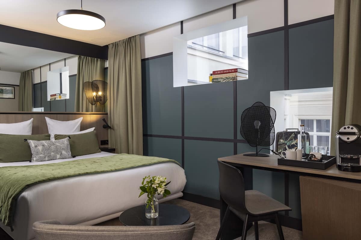 Una habitación de hotel con cama, mesita de noche, silla, escritorio y un espejo grande.