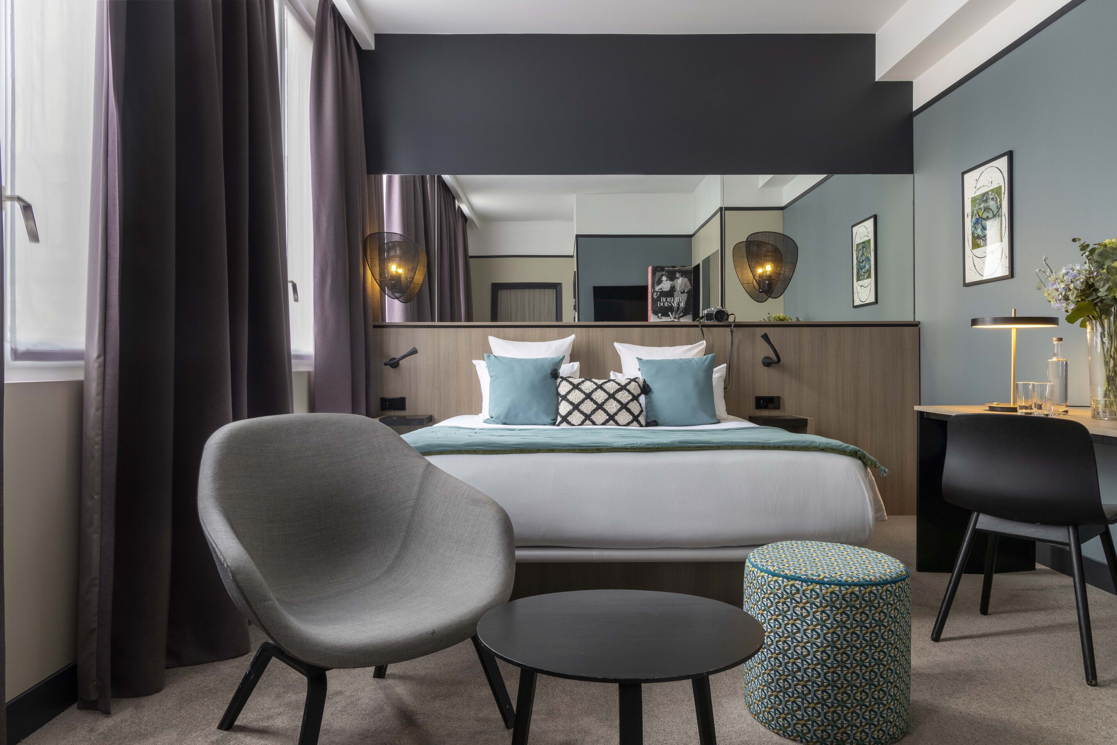A modern hotel room with a large bed, two chairs, a small table, and a mirror.