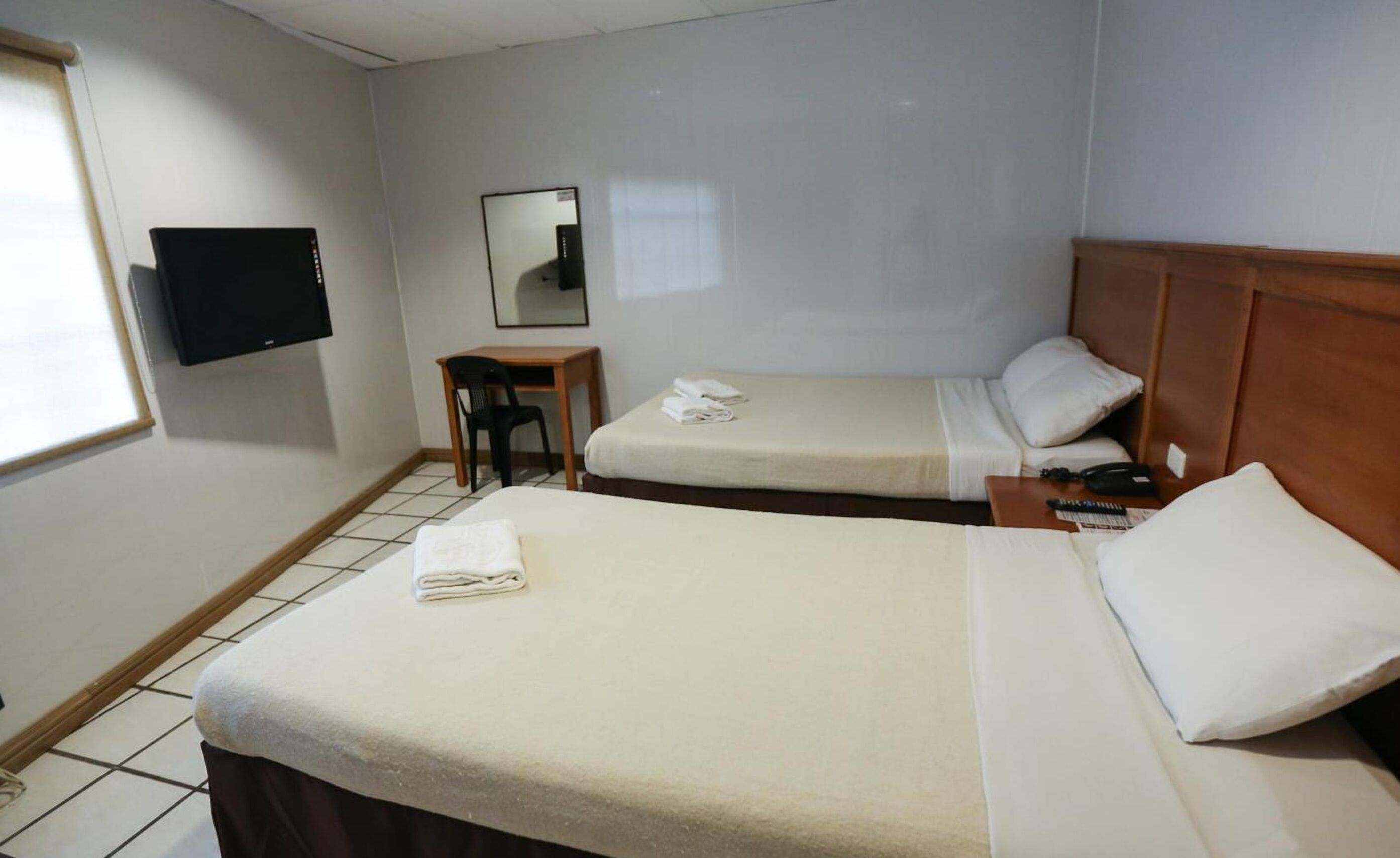 Quarto de hotel com duas camas, uma mesa, uma cadeira, uma televisão e uma janela.