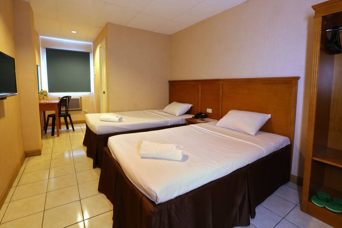 Habitación de hotel con dos camas, un escritorio con silla, televisión y armario.