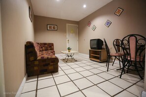 A living room with a sofa, a TV, a table with a plant, and a dining area with chairs.