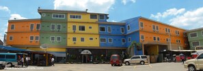 A multi-story hotel with a colorful facade, a visible entrance, and a parking area in front.