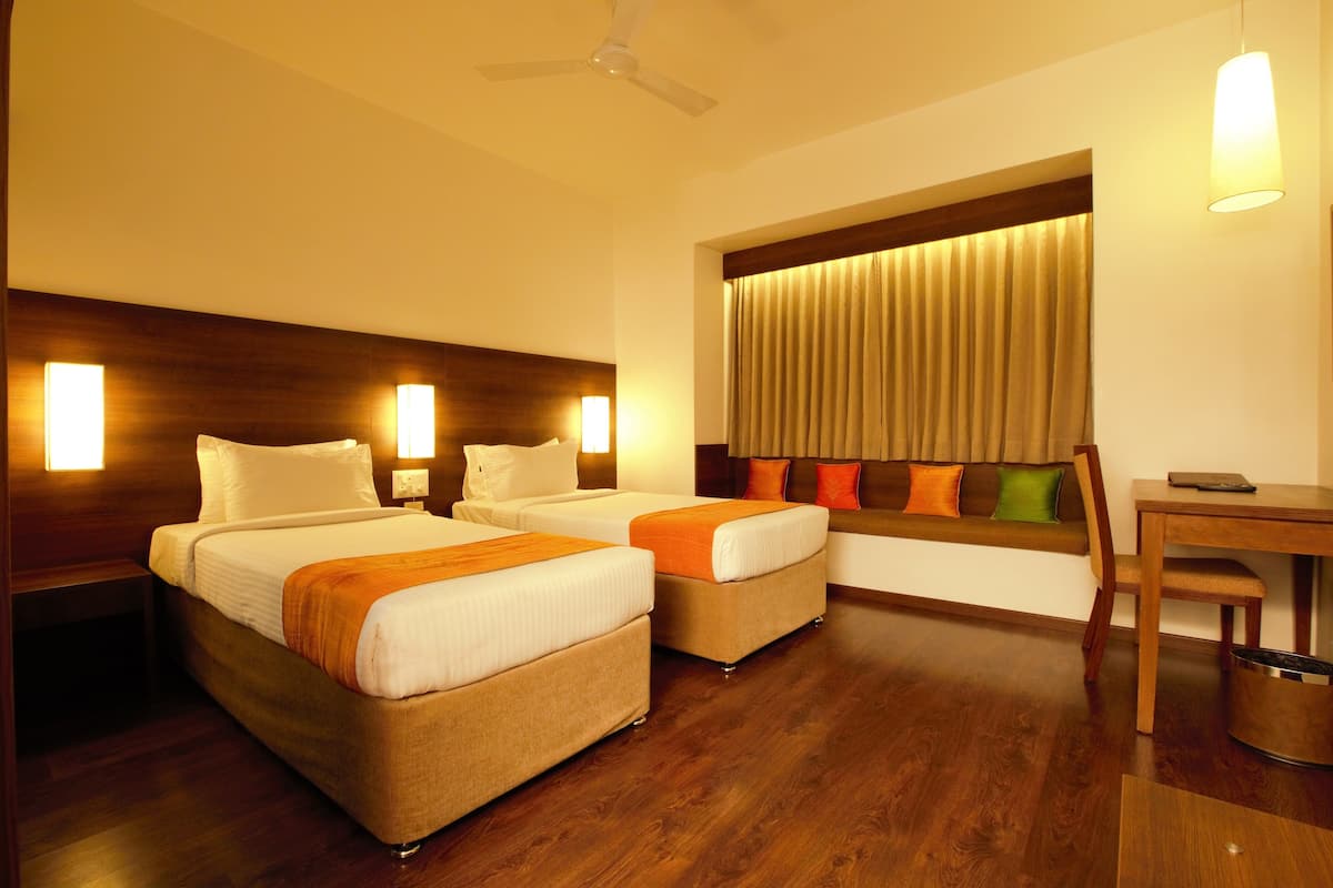 A hotel room with two beds, a desk, and a window with curtains.