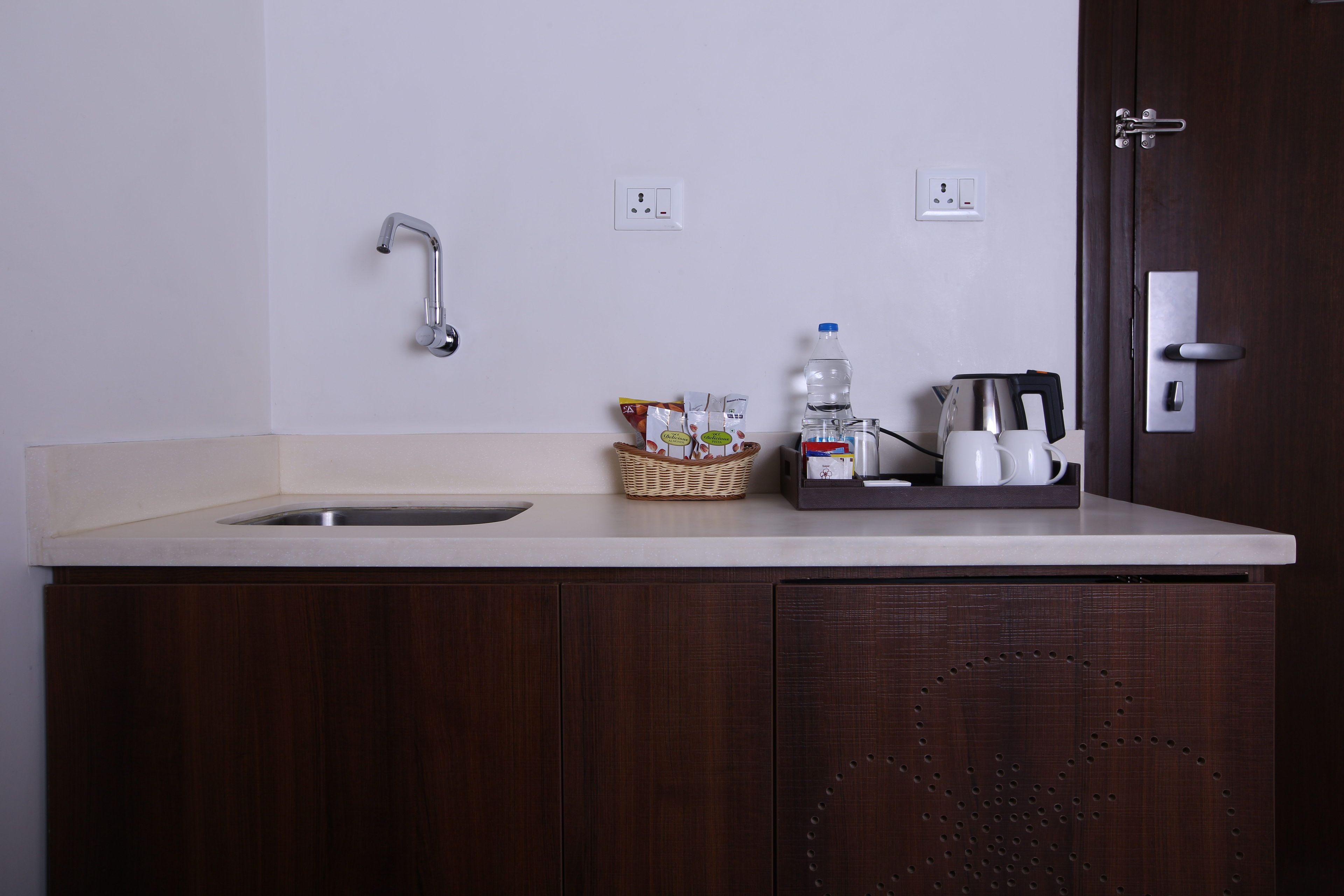 A kitchen with a sink, a faucet, a coffee maker, a water bottle, and a basket of snacks.