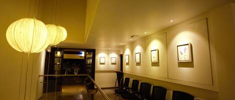 A hotel lobby with a glass railing, black chairs, and wall-mounted lights.