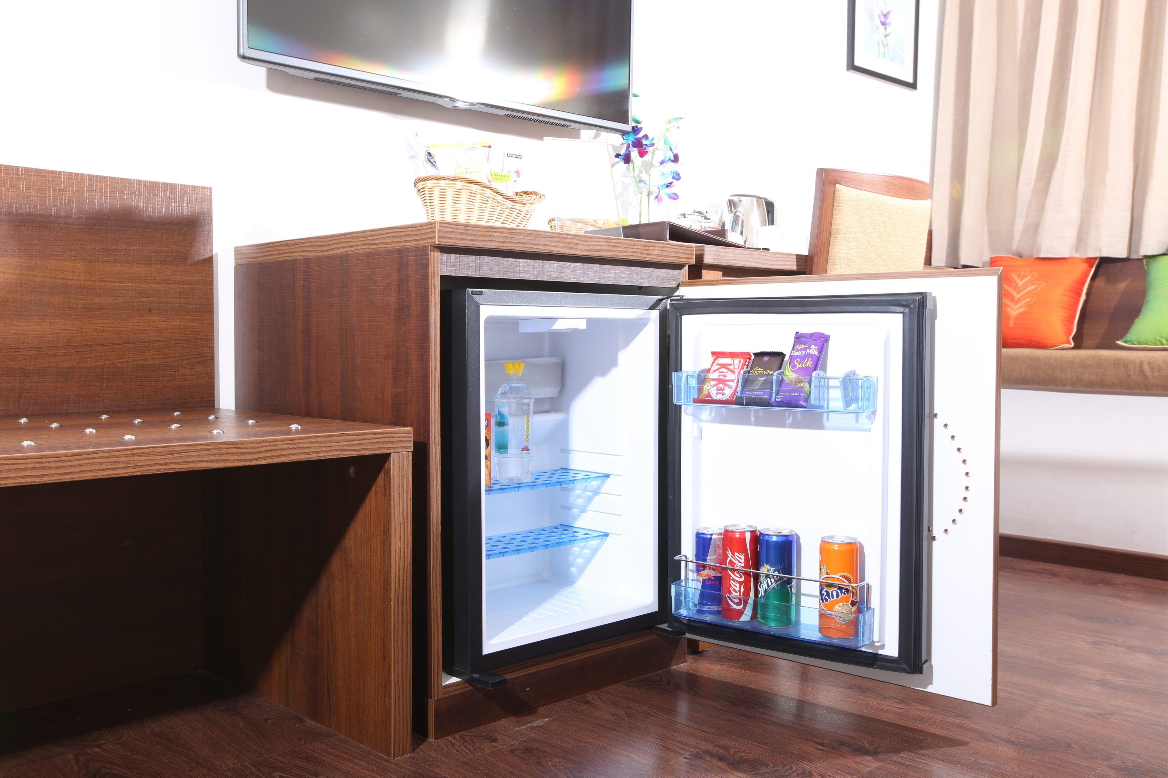 A compact refrigerator with a freezer compartment, placed in a room with wooden flooring and a sofa with cushions.