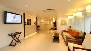 A hotel lobby with a reception desk, seating area, and a television displaying the hotel name. - Temple Tree Hotel (Bengaluru)