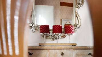 Une chaise en bois, devant laquelle se trouve un miroir reflétant une coiffeuse avec un plan de travail blanc et deux bougies rouges.