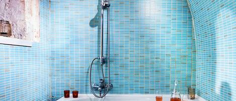 A bathroom with a bathtub, blue tiles, a showerhead, and two glasses of a pink beverage.