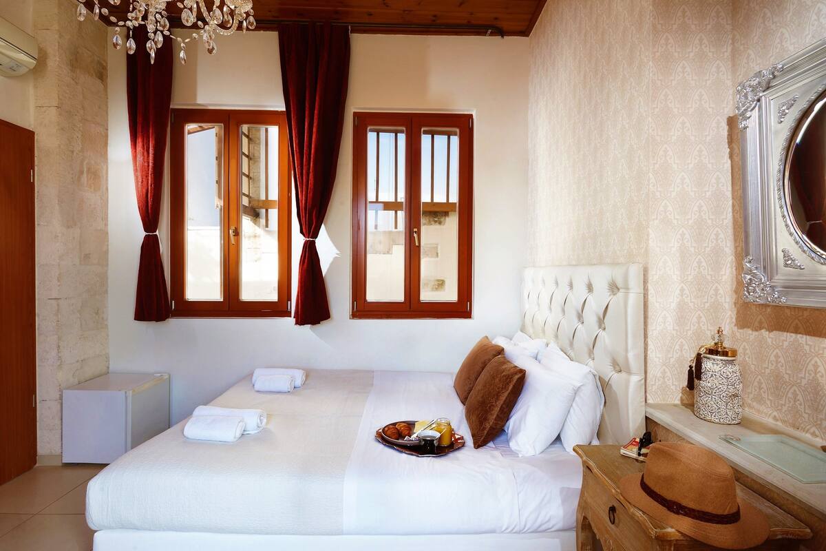 A hotel room with a bed, a small bedside table, a mirror, and a window with curtains.
