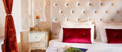 A neatly made bed with red and white pillows, a bedside table with a candle, and a wall-mounted light fixture.