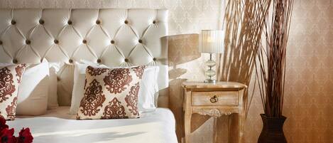 A bedroom with a tufted headboard, a bedside table with a lamp, and a vase with tall plants.