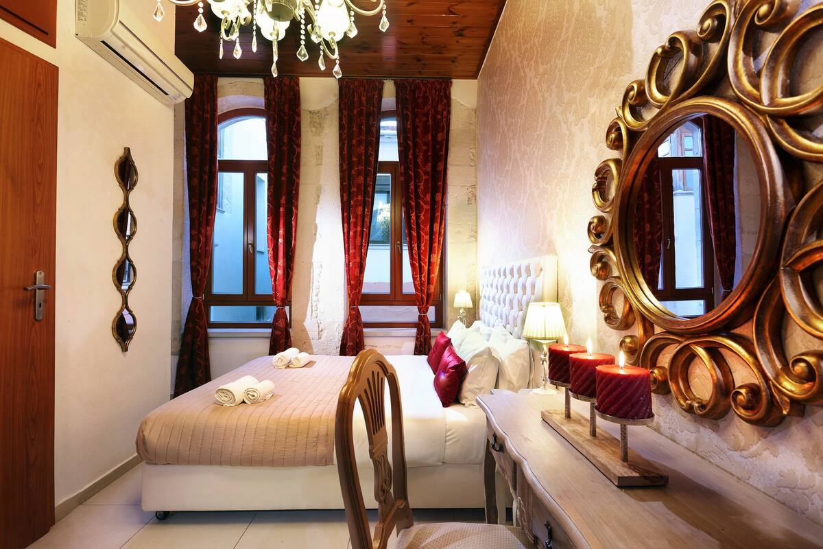 A hotel room with a bed, a chair, a vanity with a mirror, and a window with curtains.