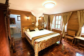 Un grand lit avec une tête de lit décorée, des murs en bois, un lustre et une fenêtre avec des rideaux.