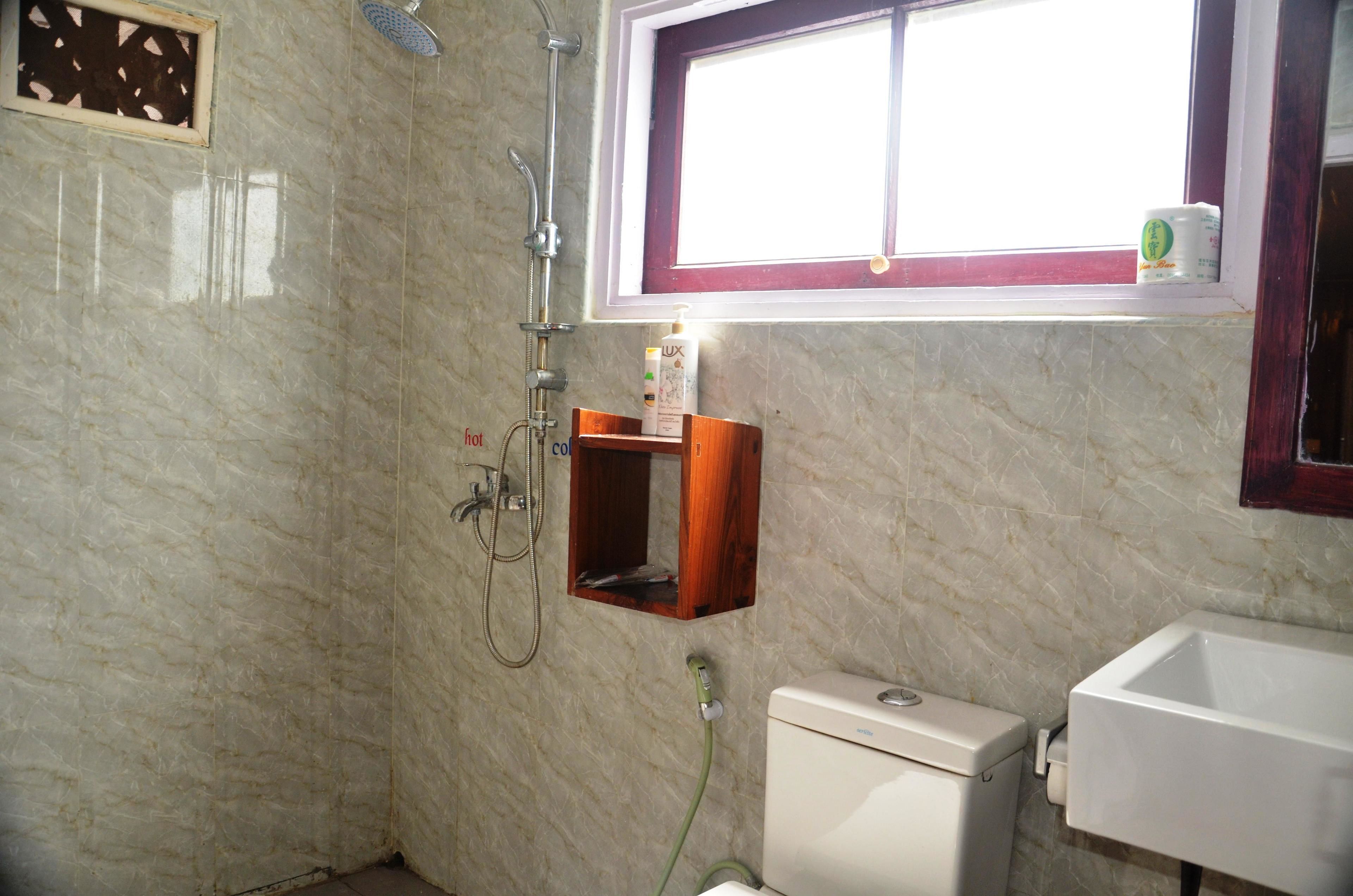 A bathroom with a marble wall, a window, a toilet, a sink, and a shower.