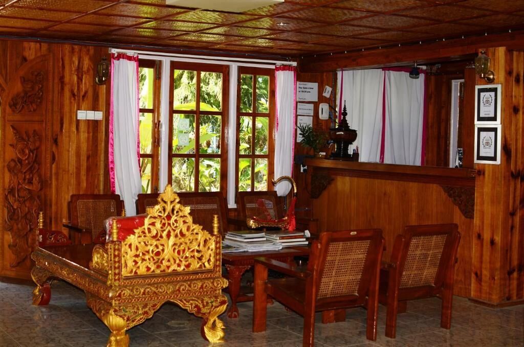 A traditional wooden room with a large ornate chair, a reception desk, and a view of greenery outside.
