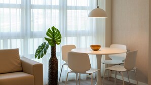 Et moderne spiseområde med et rundt bord, hvide stole, en potteplante og en hængende lampe.