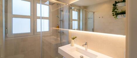 A modern bathroom with a glass-enclosed shower, a white sink, and a large mirror.