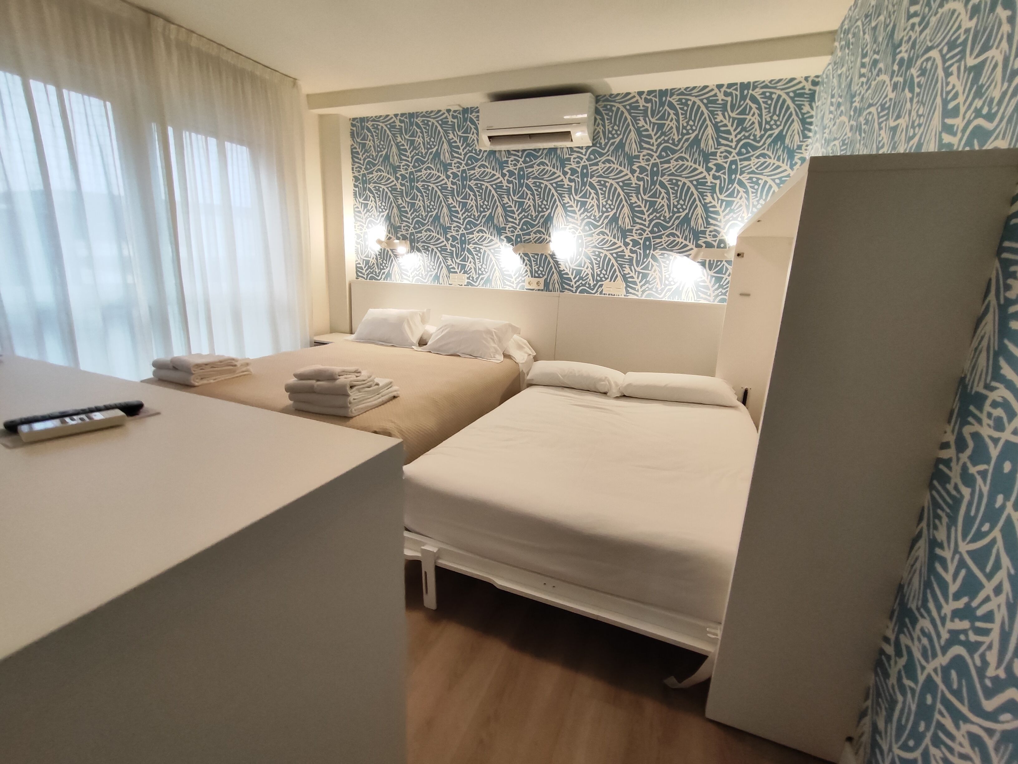 Quarto de hotel com duas camas, uma secretária e uma janela com cortinas.
