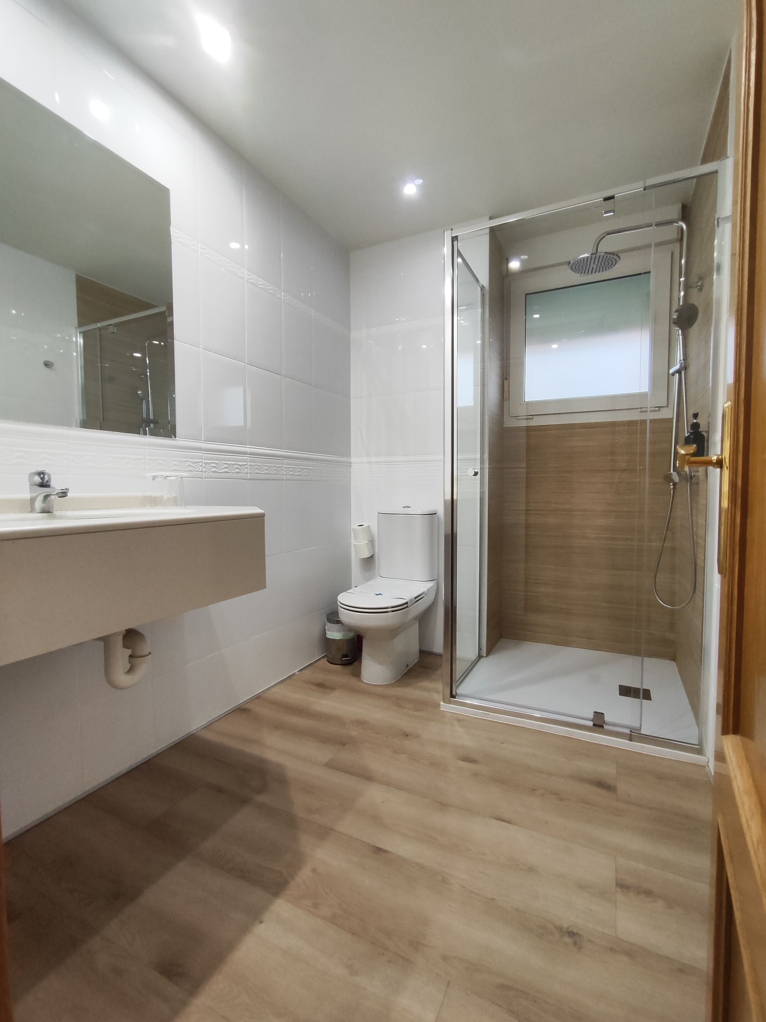 Un baño moderno con ducha de vidrio, inodoro y lavamanos con espejo.