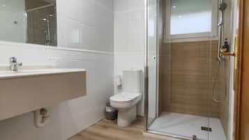 A modern bathroom with a glass-enclosed shower, a toilet, and a sink with a mirror.