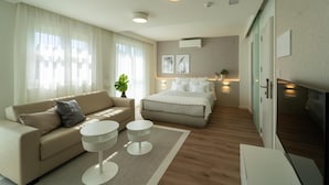 Et moderne hotelværelse med sofa, seng, to sengeborde og et stort vindue med let gardin.