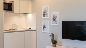 Et moderne køkken med hvide skabe, en mikrobølgeovn og et fladskærms-TV monteret på væggen. Væggene er dekoreret med indrammede botaniske tryk, og der står en lille potteplante på bordet.