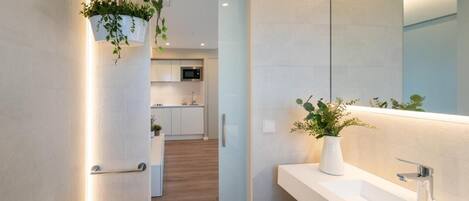 A modern bathroom with a large mirror, white sink, and a potted plant.