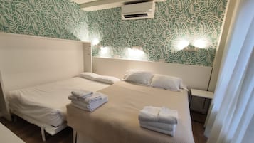 Een hotelkamer met twee bedden, een hoofdbord met ingebouwde verlichting, een split-airco en behang met een patroon.